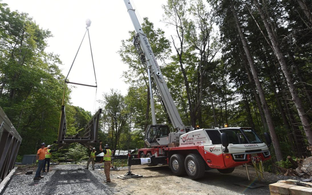 Link-Belt 120|HT telescopic truck crane lifting a pedestrian bridge section in a wooded Vermont valley