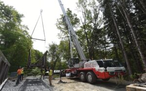 Link-Belt 120|HT telescopic truck crane lifting a pedestrian bridge section in a wooded Vermont valley