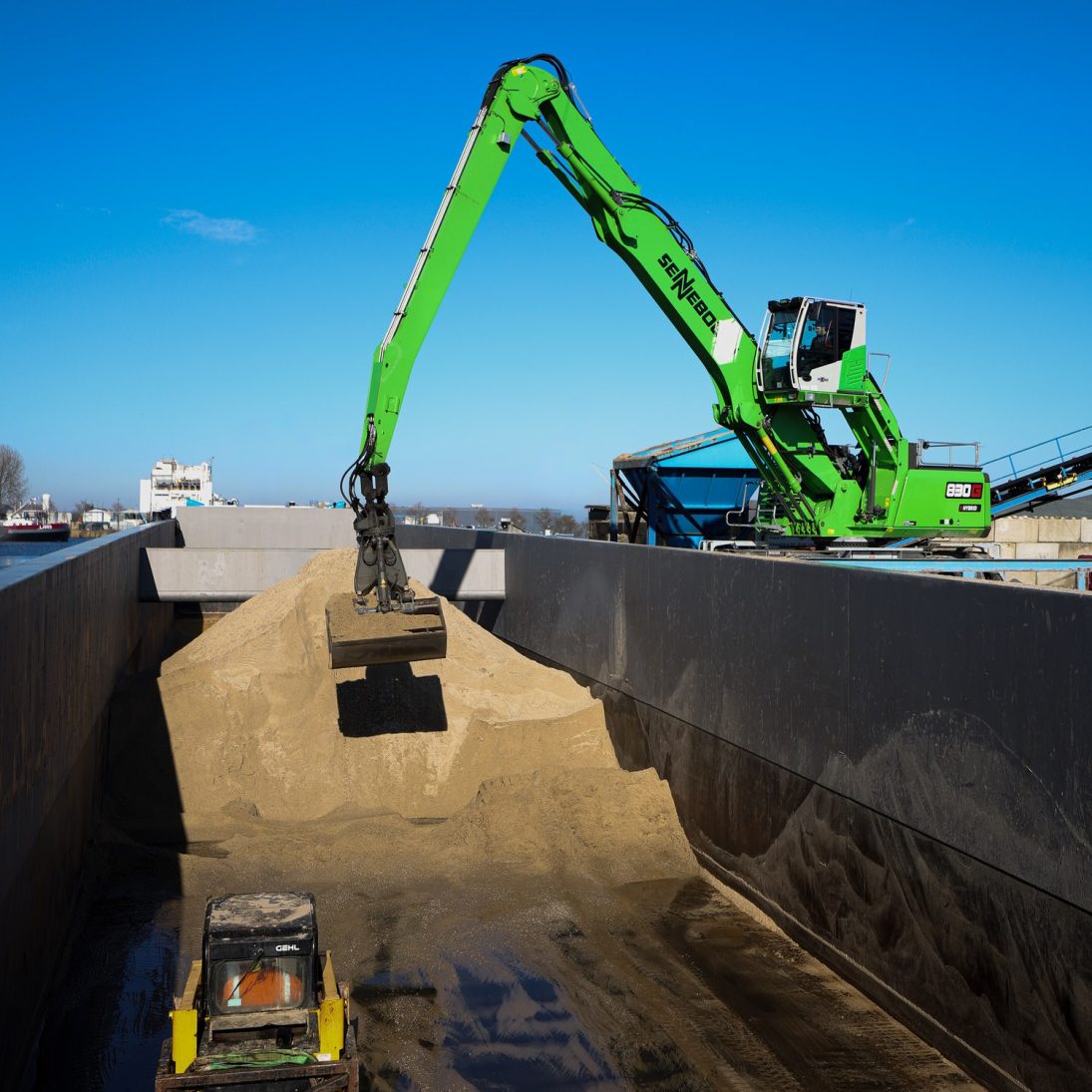 Sennebogen 830 G Hybrid reaching into the hold of a barge loaded with sand and gravel