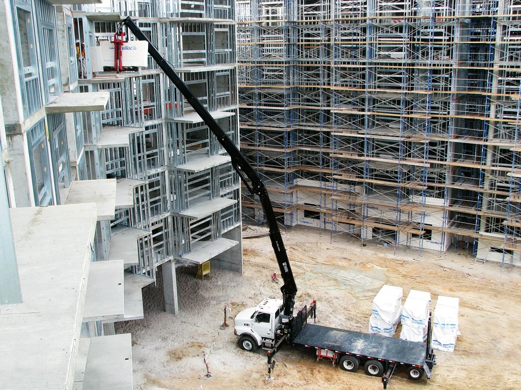 HIAB loader crane on a US flatbed truck lifting building materials into a steel-framed structure