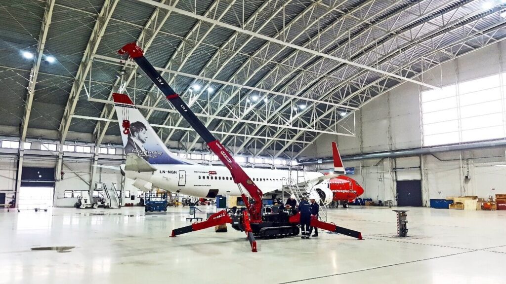 UNIC mini spider crane rigged on outriggers inside an aircraft maintenance hangar beside a Boeing 737