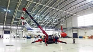 UNIC mini spider crane rigged on outriggers inside an aircraft maintenance hangar beside a Boeing 737