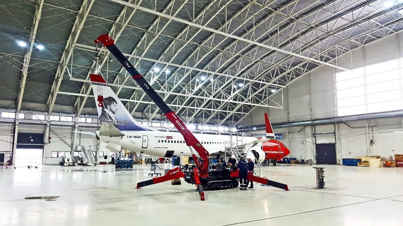 UNIC mini spider crane rigged on outriggers inside an aircraft maintenance hangar beside a Boeing 737