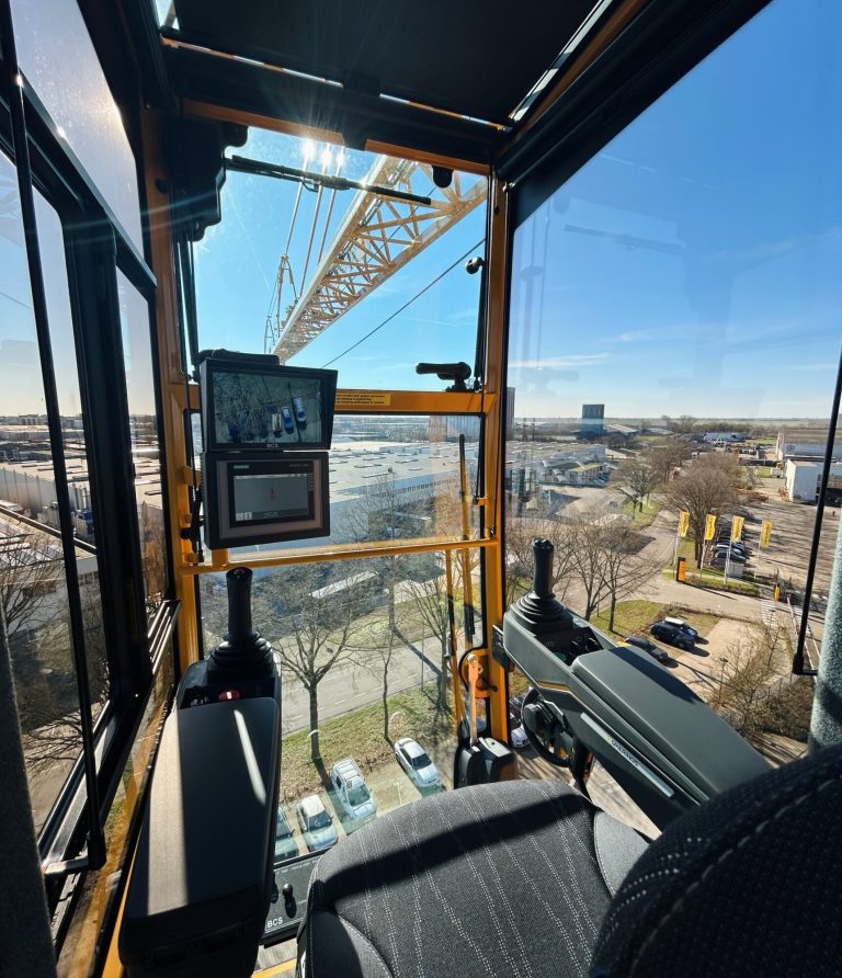 View from the operator's seat in a Spierings mobile tower crane cab showing joysticks, screens and the jib