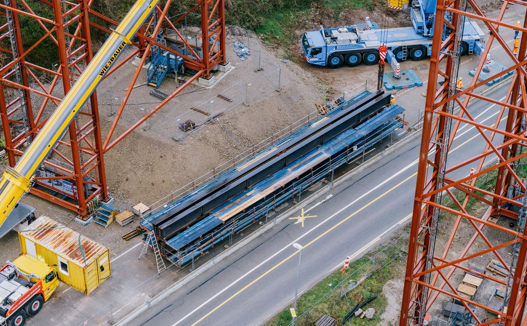 Steel bridge girders laid out beside the road with the Wiesbauer Tadano boom and an AKM mobile crane alongside