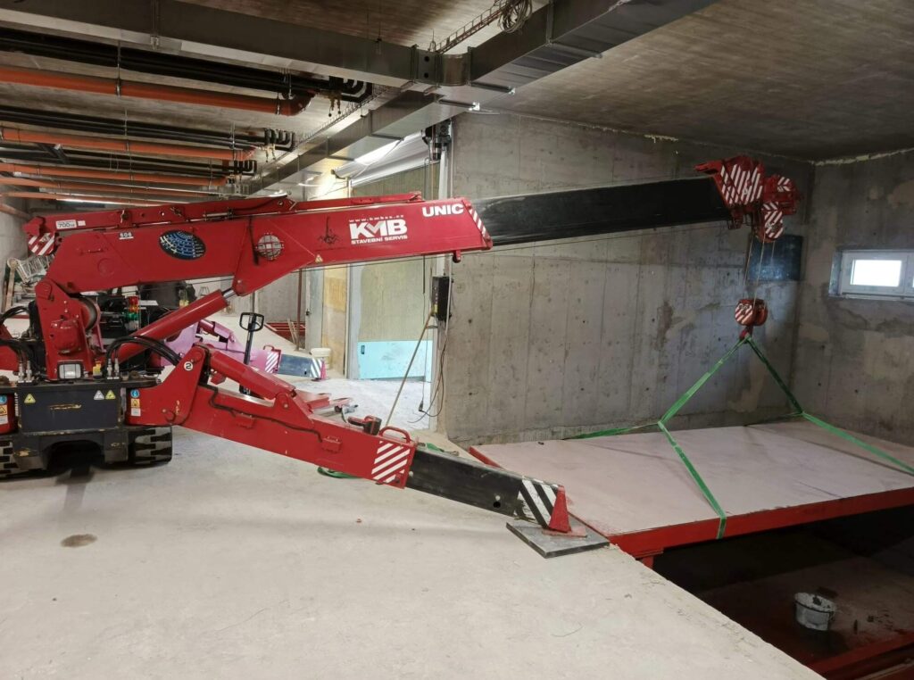 UNIC-506 spider crane lifting inside a low-headroom underground car park in Prague