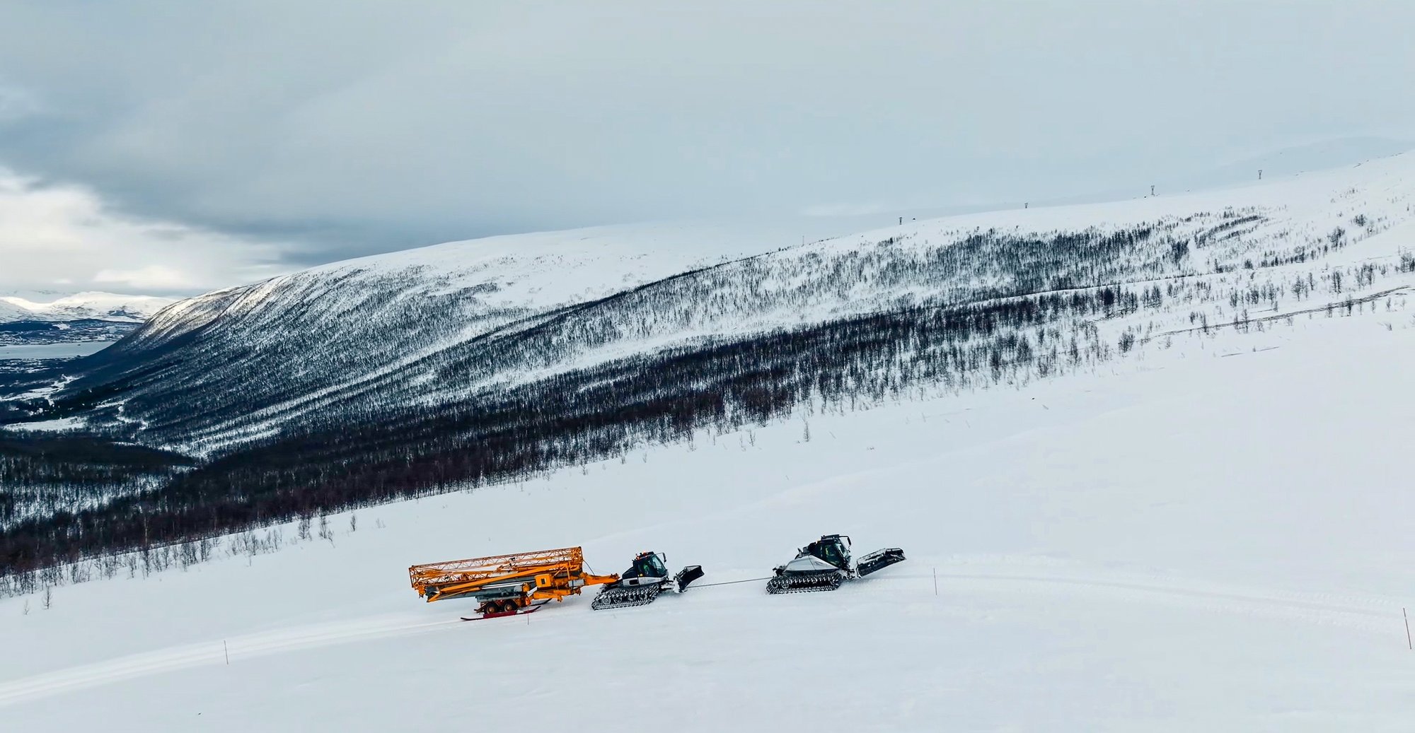 Potain HDM 40 self-erecting crane on custom skis being pulled up Floya mountain by snow groomers