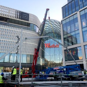 UNIC spider crane lifting a steel canopy frame outside the Westfield shopping centre in London