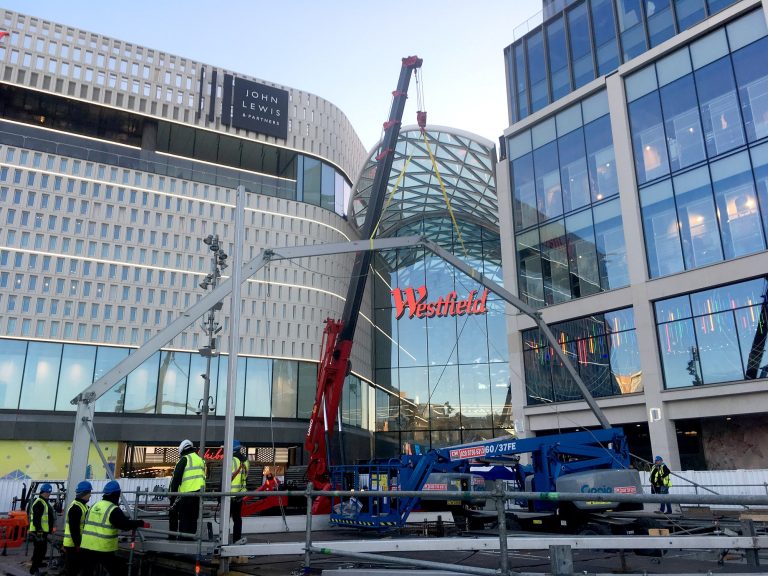 UNIC spider crane lifting a steel canopy frame outside the Westfield shopping centre in London