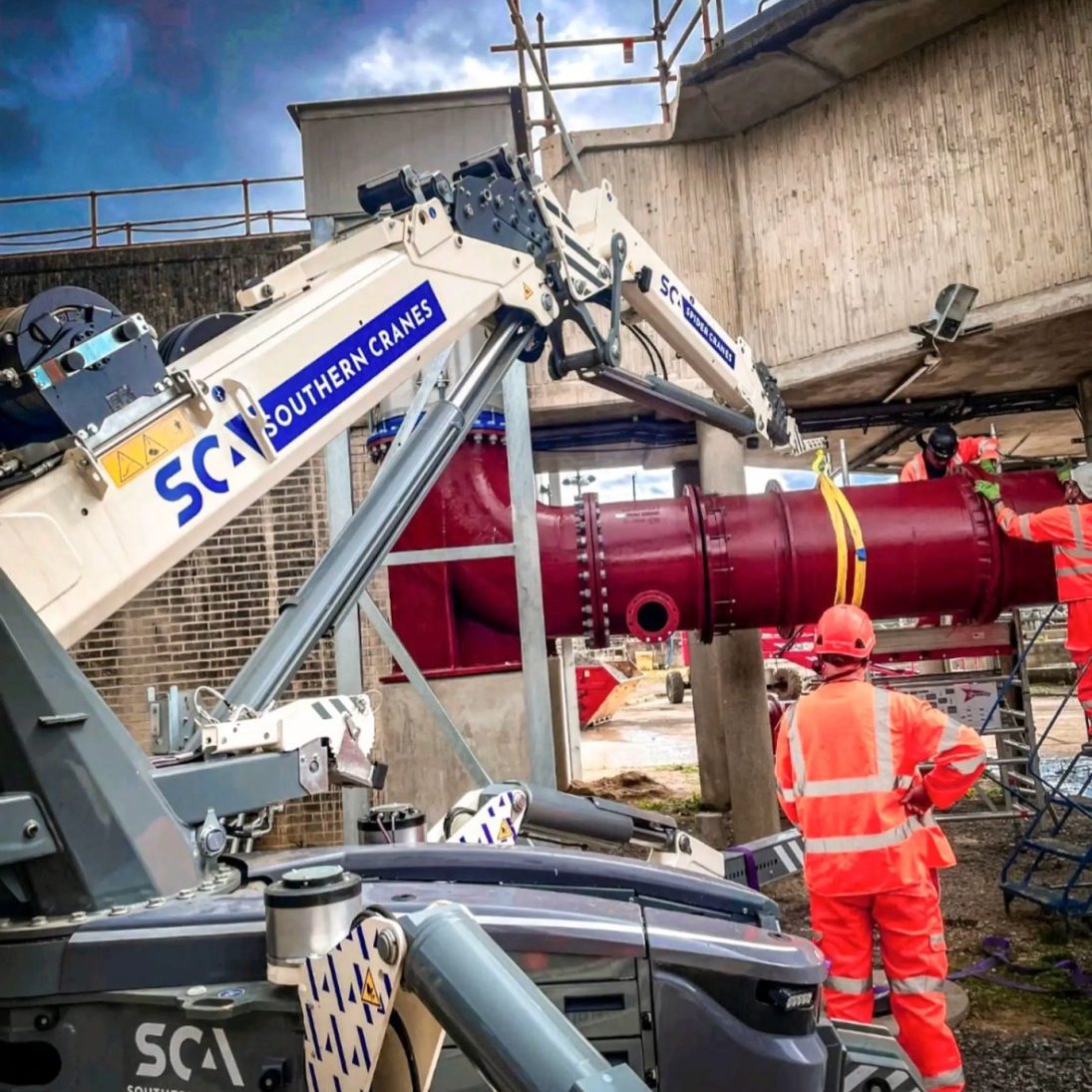 Hoeflon spider crane positioning a pipe section beneath an elevated concrete structure